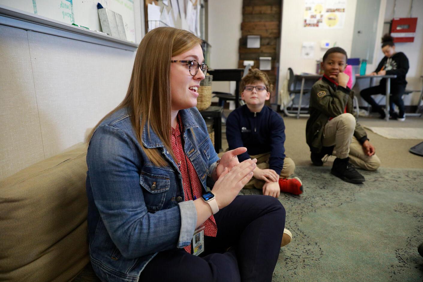 female student teacher, glasses, denim jacket, dark pants; two young male students